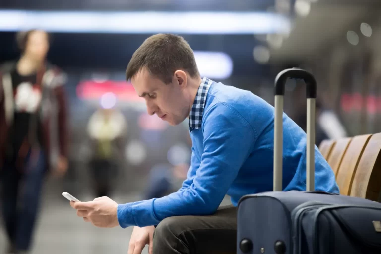 Homem sentado com mala em aeroporto olhando o celular